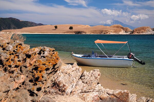 Boat parked in a crystal clear water lagoon of Ammouliani island, Halkidiki, Greece with mount Athos on the background